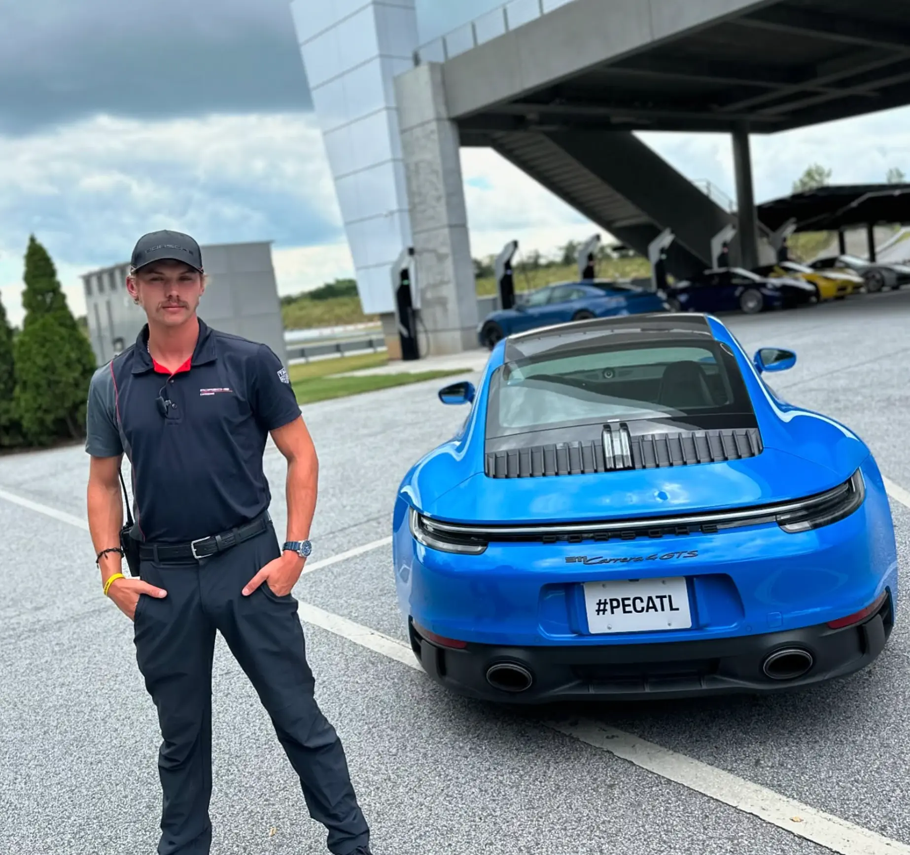 Kline Barfield as a Porsche driving instructor in Atlanta, beside a blue Porsche 911